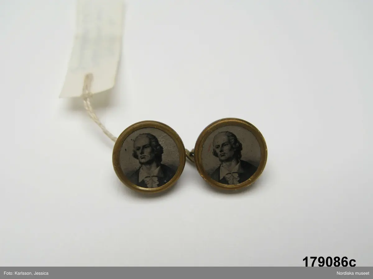Huvudliggaren (år 1929):
"179086 a-d. Manchetter fr. Gislövs by, Nöbbelövs sn, Järrestads hd, Sk.  1 par, av vitt linne m. hålsöm o spete i kanten, dubbla m. länkknappar av mässing m. infällga porträtt. I [från] Fru Hanna Jönsson, Borrby."

Bilaga:
Förteckning


Katalogkort:
Finns ej.

a-b: Manschetter. Längd: ca 20 cm. Bredd: 12,5 cm. Spets: 1 cm. Teknik: Tuskaft. Enkel utdragssöm. Maskintillverkning - spets. Handsömnad.
a-b: Ett mar manschetter av tuskaftat vitt bomullstyg. Dubbelvikt tygstycke, längd: 20 cm, bredd: 7,5 cm, med fastsydd manschettkant med rundade hörn, längd: 16,5, bredd: 5 cm inkl spets. Manschetten har broderad kantbård i yttre kant, ca 1 cm bred, maskintillverkad spets runt framkanter. Två sydda knapphål i armstycket.
/Inga-Lill Eliasson 2009-03-19