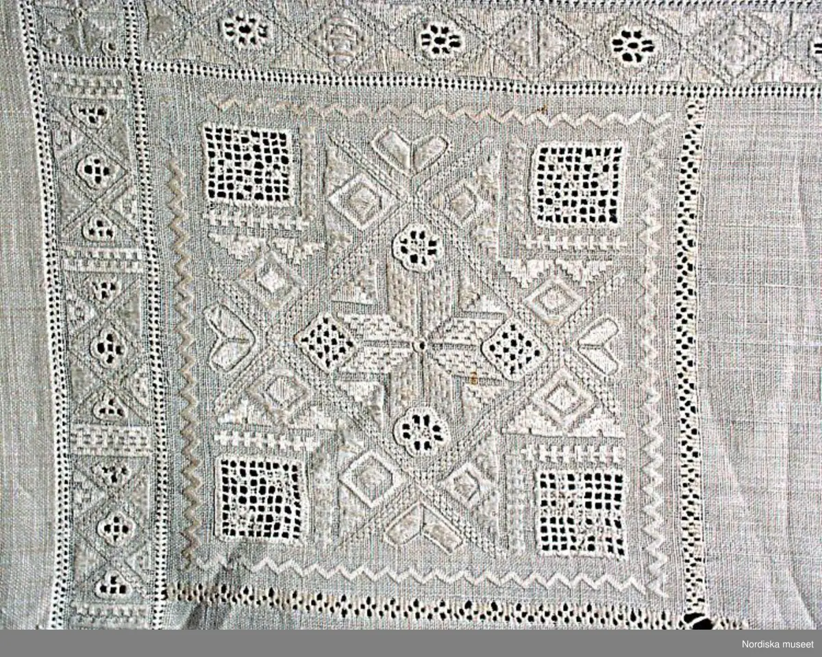 
Katalogkort:
Inga ytterligare uppgifter.

Kvadratiskt kläde i fint handvävt tuskaftat linnetyg, broderier i vitt lingarn. En 2,3 cm bred broderad kantbård  följer alla sidor. Kvadratiska hörnbroderier, 13 x 13 cm, i alla hörn. Broderierna består av rombiska, kvadratiska och trekantiga former. Utdragssöm i kanterna av bården och hörnboderierna. Broderierna utförda i rätlinjig plattsöm, utskuren söm och enkel utdragssöm.På baksidan sitter i tre av hörnen  en lagetterad hank  avsedd att fästa de dinglande hörnbroderierna i. 
Anm. Klädet har  på åtskilliga ställen stoppats  med sytråd.
Har enligt givare tillhört hennes mors faster Elin Hertzman som på 1880-talet hade gästgiveriet i Broby. Hon har enligt givaren själv, odlat, spunnit och vävt linnet. 
 Det förefller dock troligt att detta kläde har tillhört en äldre generation innan Elin H. ägde det.
Utdrag ur Svensson Sigfrid, (1935). Skånes Folkdräkter, en dräkthistorisk undersökning 1500 - 1900. Stockholm: Nordiska Museets Handlingar: 3, sid. 262 - 263: "Härmed kan sammanställas Linnés uppgift från Göinge: 'Torrklädet' är et linne armkläde, wid kanterna genombåradt och sydt samt med spetsar kantadt och med wippor i hörnen utsiradt'. Dessa benämningar - 'näsduk', 'torrkläde' och 'armkläde' - förekomma i bouppteckningarna redan vid 1700-talet början och åsyfta tydligen då en duk, som burits på armen eller hållits i handen...Från Ö. Göinge omtalar Eva Vigstsröm, att till fästmögåvorna också hörde en 'kinnaklud' och enligt beskrivning var denna av fullkomligt samma utseende som armklädet. Om dess användning säges: 'Denna klut bands helt utbredd öfver brudens hår, då hon red eller åkte till kyrkan.' Samma bruk har förekommit i Ingelstad: 'Under resan till och från kyrkan hade bruden öfwer locken, liksom öfwer kluten, ett 'hyeklä', ett fyrkantigt tygstycke af linne med genombrutet arbete.'. Enligt Wistrand användes samma plagg även vid kyrkobesök och resor och Svanander omtalar hyeklädets användning till sorgdräkten, fig 242. Att armkläde och hyekläde förkomma samtidigt i bouppteckningarna torde bero på en senare differentiering. Ett och samma slags linneduk har kunnat användas som förningsduk, 'bokkläde' och 'gudmoraklut' (som bars av faddrarna ovikt och fäst under hakan på samma sätt som hyeklädet)."
Lästips: Håkan Nilsson, Röepäls, klut och skörtatröja, s. 28-41.
Östelens folkdräkter, Ystadiana 2000.  Ystads Formninnesförening. Ystad 2000.
/Berit Eldvik 2010-10-18
