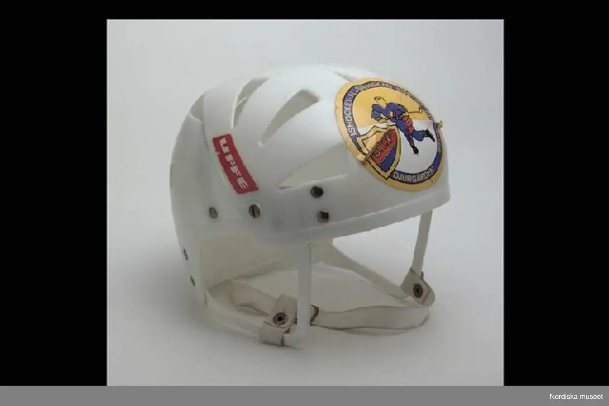 Inventering Sesam 1996-1999:
L  21   H  19 (cm)
Ishockeyhjälm, av gjuten vit hårdplast, genombruten, hopsatt med nitar av gulmetall, ¿ronbyglar med reglerbart hakband av plastad, kraftig väv med tryckknapp, ingjutet baktill: "ABC-FABRIKERNA / KUNGÄLV SWEDEN". 2 st påklistrade etiketter; r¿d etikett med vit text: "UFFE" och rund etikett med bild av ishockeyspelare samt sk¿ld med text: "D.I.F." och "ISHOCKEYALLSVENSKAN 1966-67 SUPPORTER  DJURGÅRDEN".
En bygel trasig.
Anna Womack mars 1998