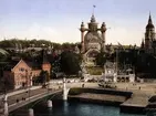 Stockholmsutställningen 1897. Vy från Strandvägen mot utställningen med Djurgårdsbron i förgrunden. T h Nordiska museet, i centrum Industrihallen, ritad av arkitekt Ferdinand Boberg. Kolorerat fotografi.