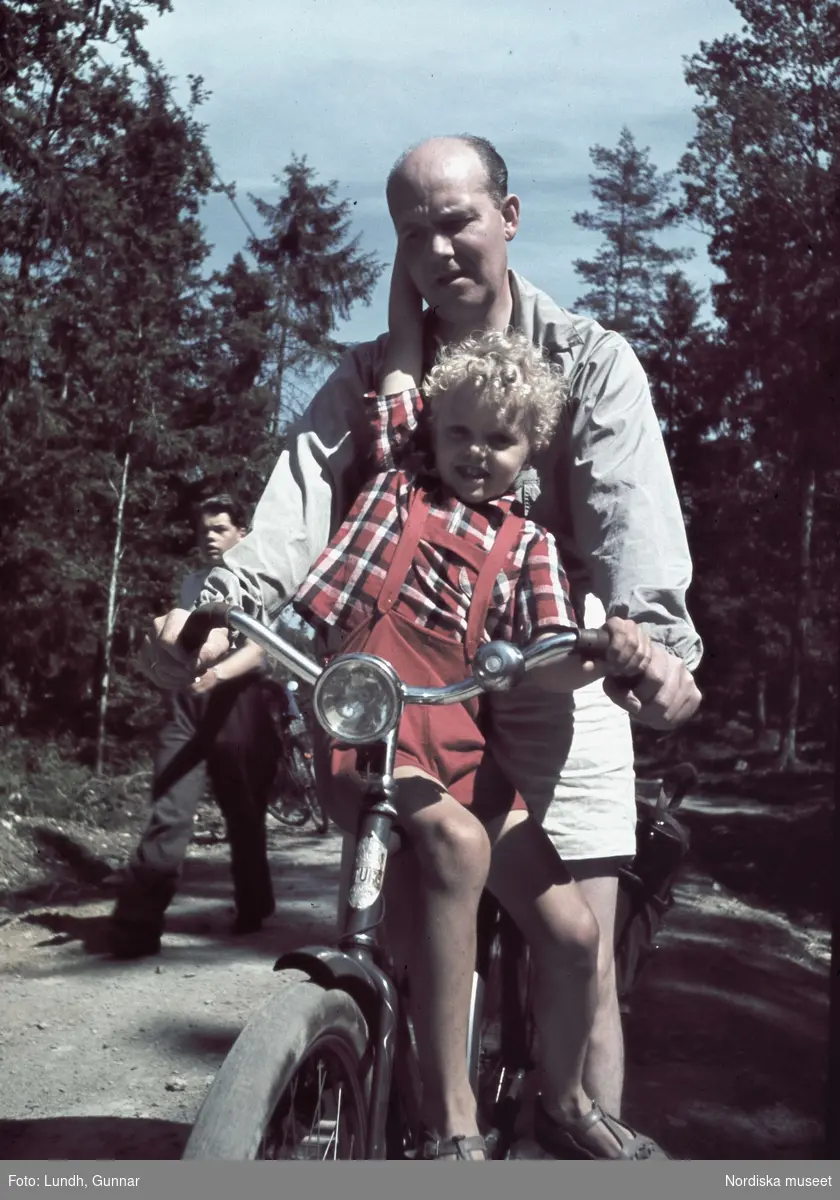 Man på cykel, liten pojke sitter på cykelramen.