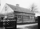 Lunderhaga gård i Fleringe socken, Gotland. Låg byggnad av liggtimmer med lerklinad gavel. Framför huset ett staket med öppnad grind.