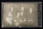 Gruppbild, familjeporträtt. En man, två kvinnor och två barn. Text på baksidan 