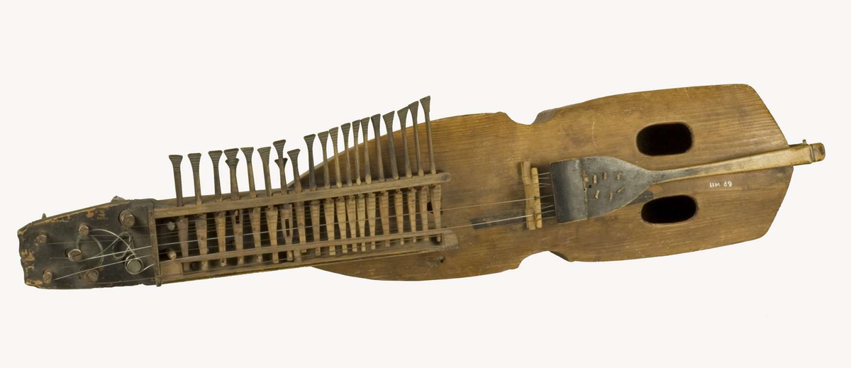Nyckelharpa, s.k. kontrabasharpa. Korpus bestående av skrov täljt av granträ med lock i granträ. Nyckellåda av lövträ. Nyckellådans överliggare dels intappad dels fastskruvad med järnskruv. Dubbla nyckelrader med i övre raden 19 nycklar och i den undre två. Harpan har tre melodisträngar och ev. bordunsträng. Stränghållare av svartmålat lövträ fastbunden med snöre. Stämskruvar och nycklar av svartmålat lövträ.