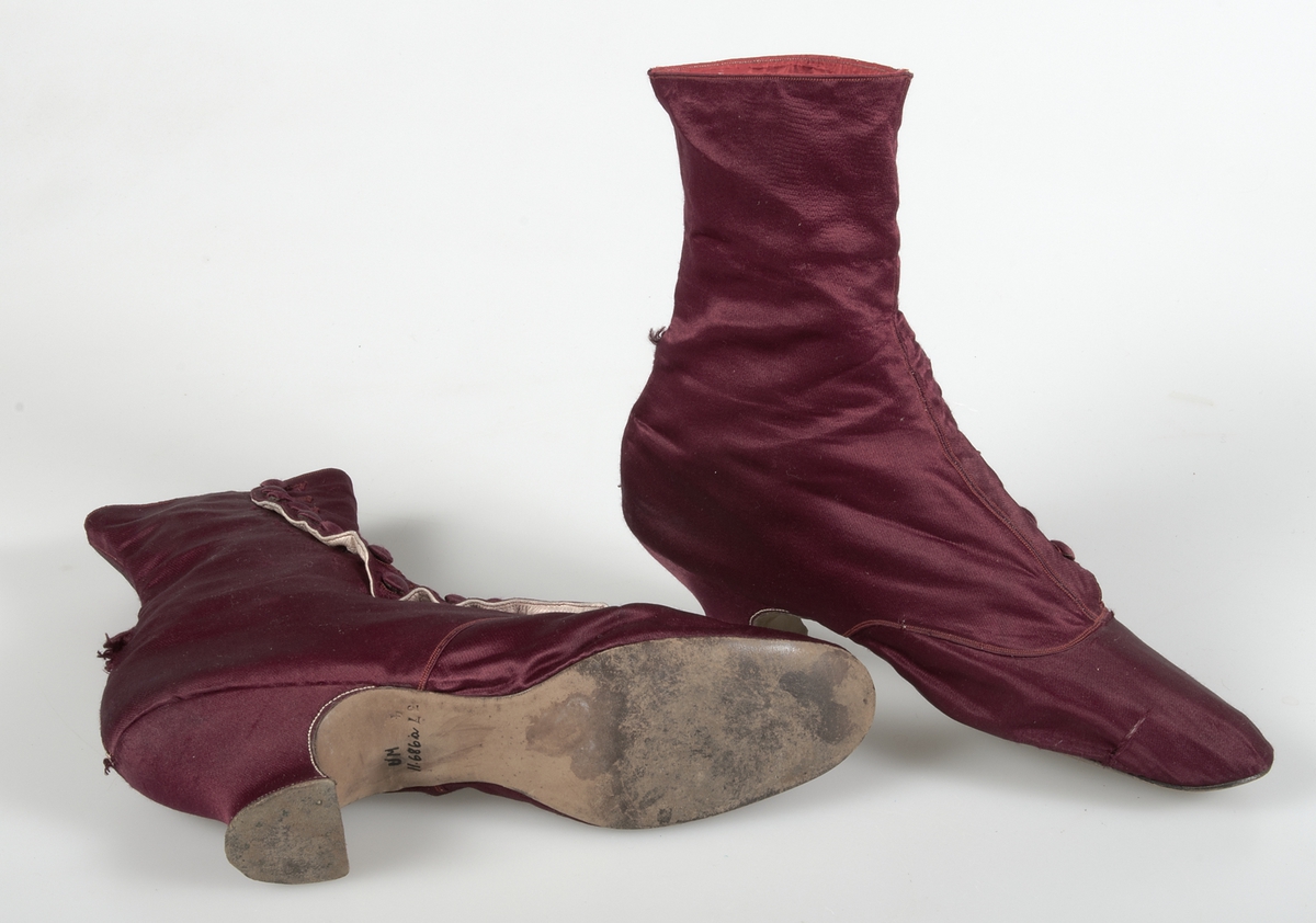 Kängor av vinrött siden. Knäppt med 14 klädda knappar. Brun lädersula. Fodrade med vit lärft, vitt skinn och rött siden.