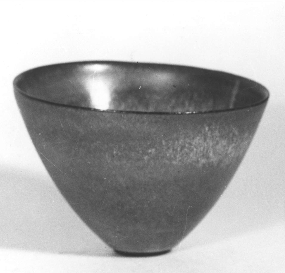 Skål utförd av Ingrid Atterberg omkring 1950. Av sintergods med ljus, krakelerad glasyr i beigeljusblått. Mynningen ej parallell med bottnen.