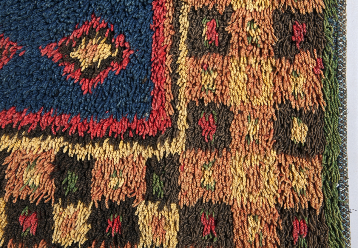 Prydnadsrya i två våder, hopsydda kant i kant. Botten i korndräll med varp av blått s-tvinnat lingarn 11 tr/cm och inslag av mörkbrun s-spunnen ull 7½ inslag/cm. Nockor av en tråd tvåtrådigt z-tvinnat hårdtvinnat ullgarn, knutna med giordesknut över 4 varptrådar med 4 varptrådar mellan nockorna och 4 inslag mellan nockraderna. Nockorna syns ej på baksidan.

Mönster: Stort blått mittfält avgränsat mot bården av en röd, en grönbrun och en gul smal linje. På det blå mittfältet, utmed sidorna romber av rött, grönbrunt och gult. Bred bård av schackrutor i grönbrunt, gult och rosagult. Gröna, röda och gula prickar i rutorna. Ytterst smal grön rand.