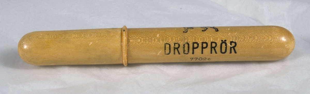 Förpackning för dropprör. Rörformigt i ljust lackerat trä. Två stycken som träs i varandra. Ett tryckt lejon i svart. Därunder i svart tryckt text: DROPPRÖR 7702 c, Apoteket Lejonet, Upsala. Stora Torget 5. 