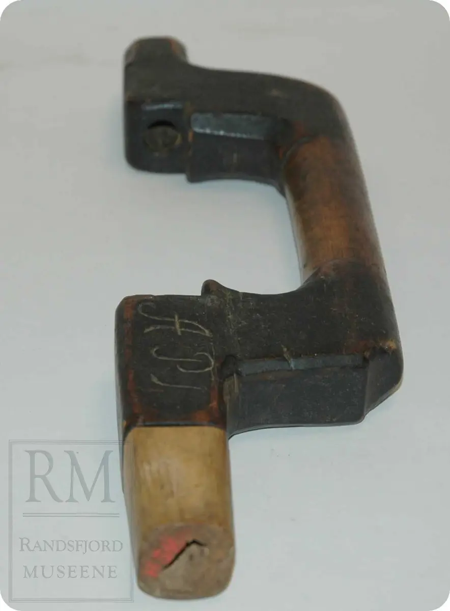 Et stykke tre. Formet som en bue med rette kanter. Glatt. Toppen mangler. Utskjært APM.