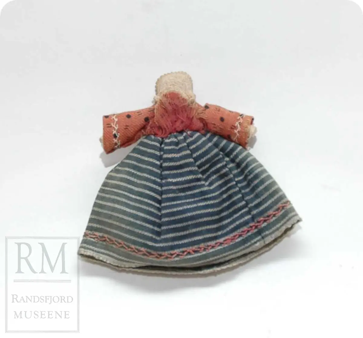 a: Liten dukke i stoff. Flatklemt. To underskjørt, skaut. b. Papir med håndskrift stilet til "Student Nielsen" og merket "Fra en Venninde paa Røros 1865" Tekst: Agtværdige Herr Person! Saasom, dasom og eftersom jeg i disse Dage er berøvet mine fordums gode Talegaver maa jeg i dets Sted gribe til Pennen, for paa den Maade, at faa sige Dem, hvad som egentlig ligger mig paa Hjerted. Det er blit mig fortalt, at De om nogle Dage, agtes at drage ned til Hovedstaden. Den samme Tour staar ogsaa for mig, men at jeg alene kan begive mig afsted skjønner De nok er en Umulighed. Derfor kjære Student, er det min inderlige Bøn til dem, om jeg kan faa slaa Følge med. Jeg ser dem an for at være en ret paalidelig og god Reisefælle, og vover jeg da at gjøre Dem dette Spørgsmaal. Haaber da at De unskylder min Nærhed, slutter jeg disse Linier. Det er mig meget om at gjøre at jeg allerede i Dag kunne faa et par Ord til Svar. Modtag den bedste Hilsen fra Deres hengivne og forbundne Simonette"