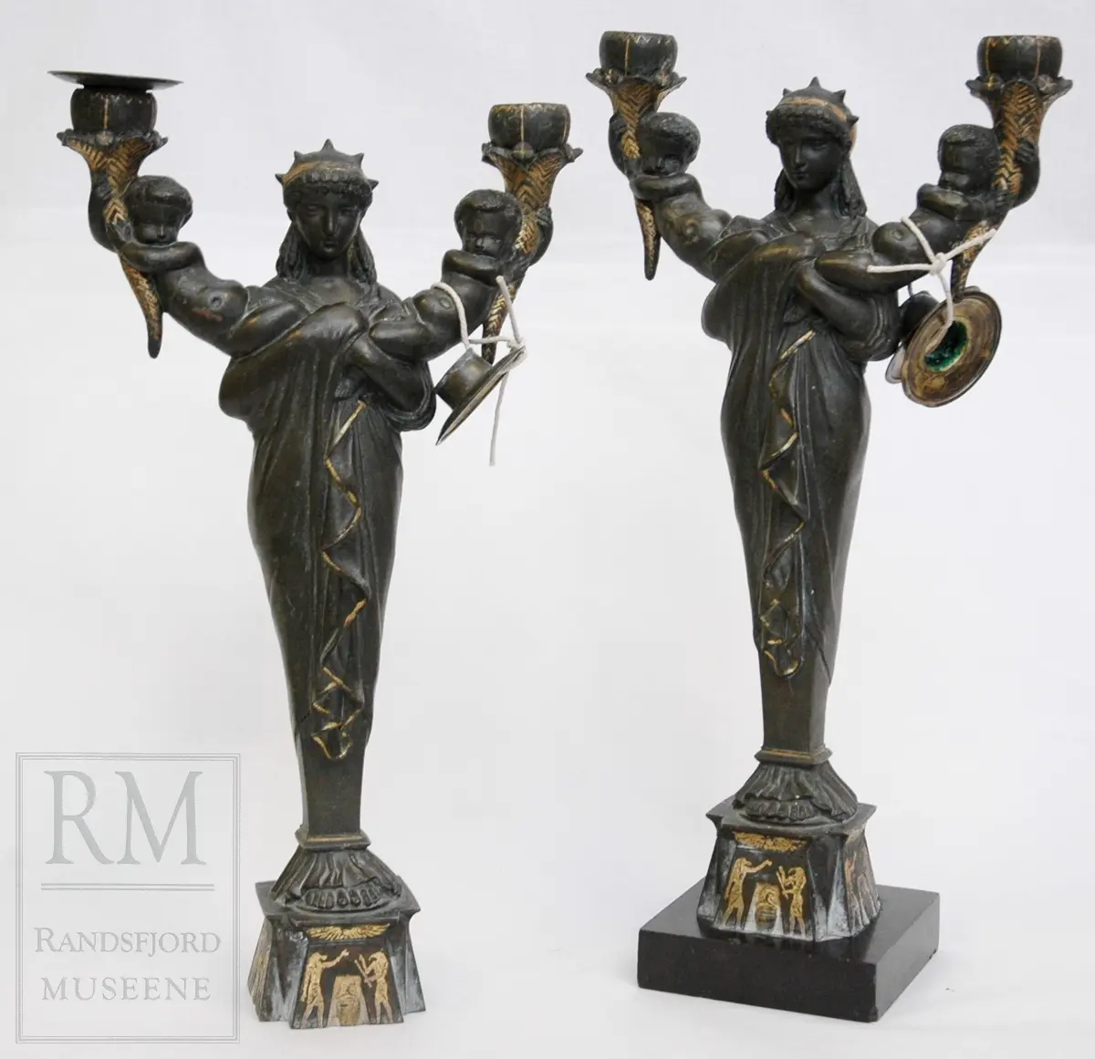 Kvinnefigur på sokkel, med ett barn i hver arm. Barna holder hvert sitt horn (?) med lyseholder. Noe forgylling. Løse lysmansjetter. b) mangler sokkel.