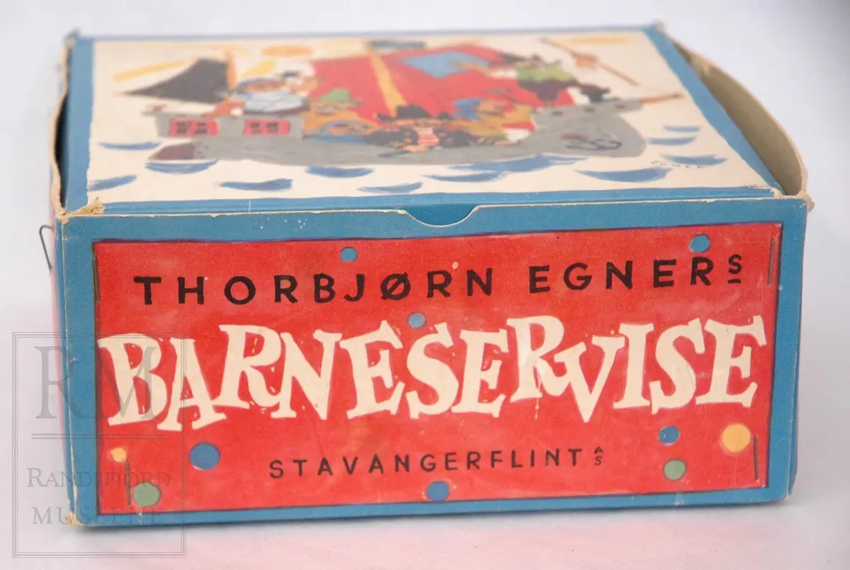 Flat tallerken, dyp tallerken og kopp i hvitt steintøy med fargerik dekor: motiver fra "Kardemommeby" av Torbjørn Egner. Eske med Egners tegninger og teksten til sjørøvervise.