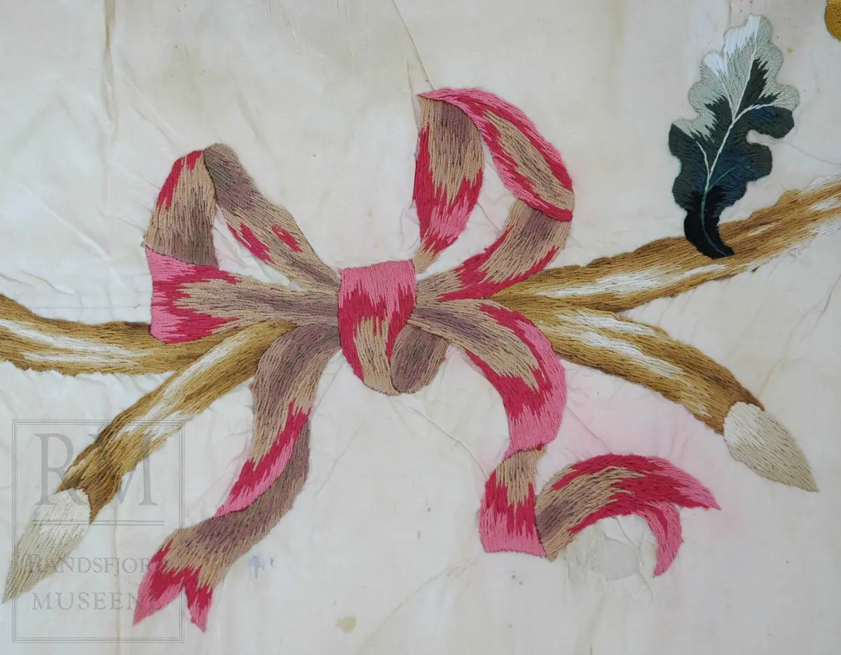 Fane av hvit silke. Løpegang på den ene siden har revnet. Brodert tekst, samt eikebladskrans med sløyfe omkring to gevær med påhengende krutthorn.