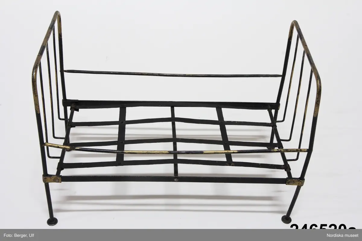 Inventering Sesam 1996-1999:
a) Järnsäng av enkel modell, av järnstänger i svart och guld, höga gavlar, botten av plåtband. L 41 cm, B 22 cm, H 39 cm
b) Madrass av röd- och vitrandig bomull, stoppad med tagel, röda puskor. L 40 cm
c) Bolster av röd- och vitrandig bomull, stoppada med fjäder. L 36 cm
d) Kudde (långkudde) av röd- och vitrandig bomull, stoppad med ull (el. liknande). L 20,5 cm
e) Kudde av röd- och vitrandig bomull, stoppad med ull (el. liknande). L 13,5 cm
Till sängen hör sängkläder inv.nr 246.521-246.527.
Leif Wallin april 1997