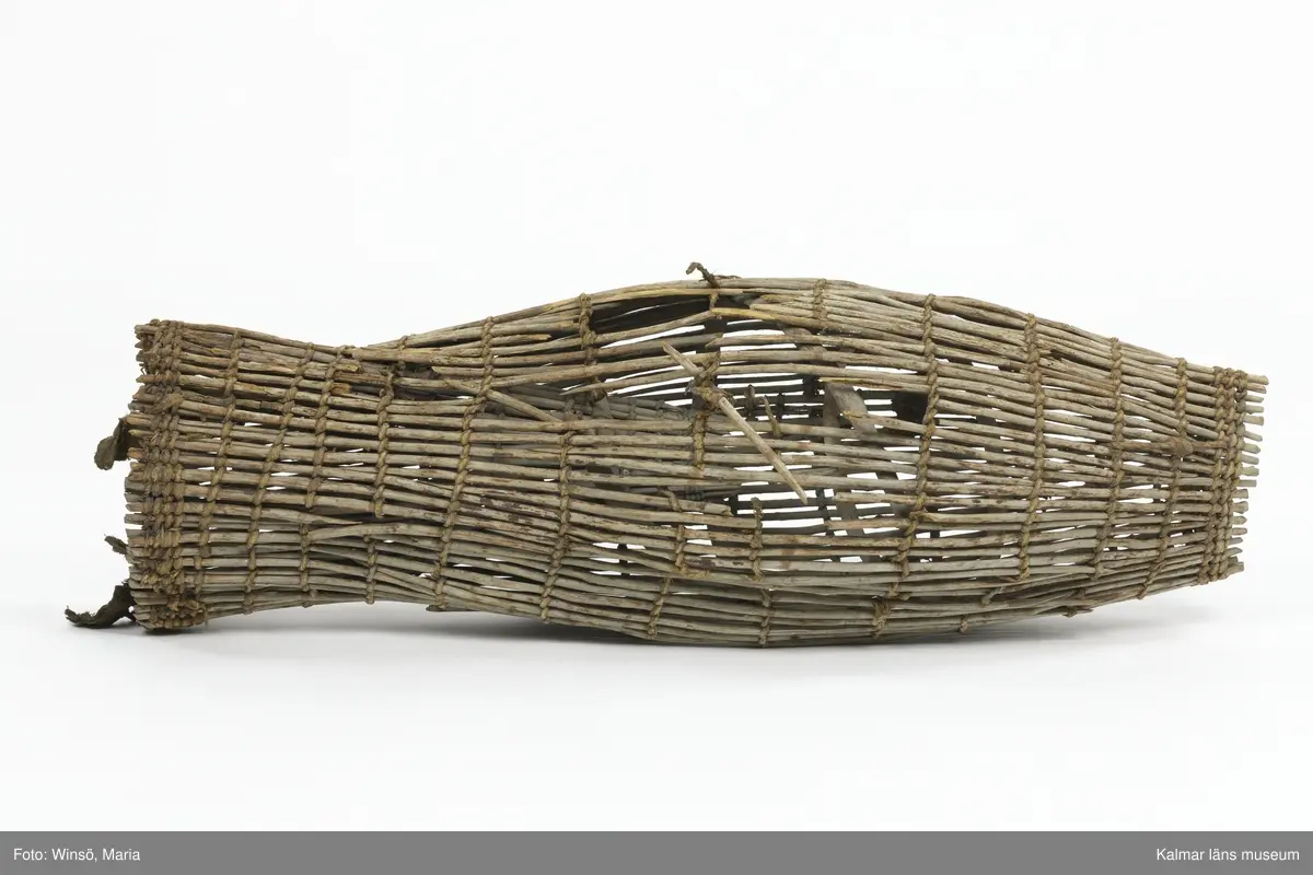 KLM 28553. Mjärde, dialektalt "ålhomma". Användes vid fiske av ål. Av vidjor sammanflätade med kedjor av rep. Spolformad och med strutliknande inredning i den cylindriska änden. I ena öppningen tygstycken. Lagad med rep på några ställen. Större skada på ena sidan.