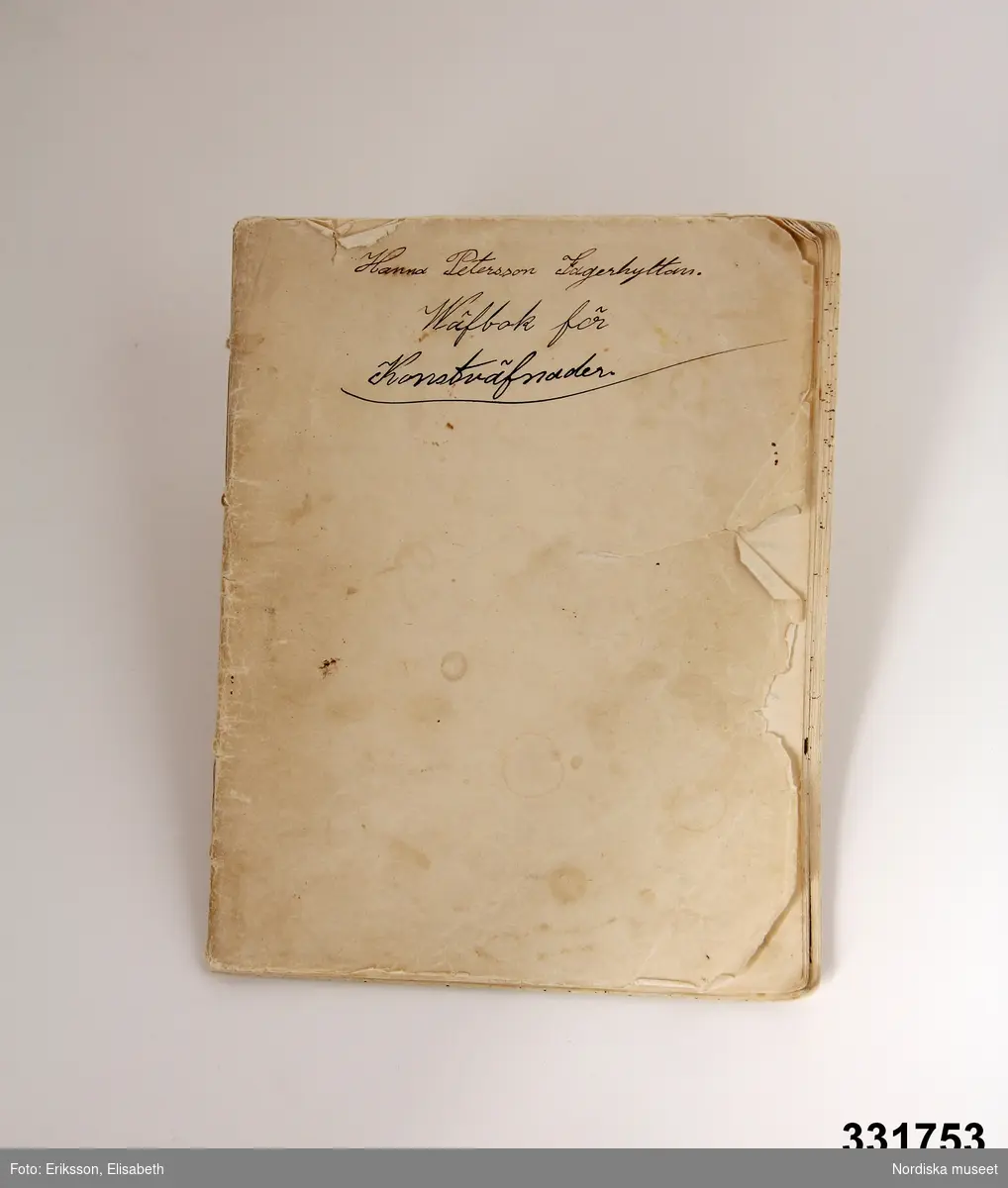 Vävbok, handskriven på olinjerat papper ihopsytt i ryggen. Omslag av samma papper som inlaga. Text på omslaget "Hanna Petersson Lagerhytttan / Wäfbok för Konstväfnader".  Boken innehåller 80 sidor med vävbeskrivningar, vävnotor och kommentarer kring uppsättning, material, teknik etc.. Ex. på rubriker "Snörenas mått till väftalen / Dubbel mattväfnad / knytnotan för drällhväfnader / Stramalj / Rosengång solfnotan / Kädningstyg med fina hoppor / Lappmattor." m fl.

Anm. Omslaget naggat och trasigt.
/Anna-Karin Jobs Arnberg 2013-05-30