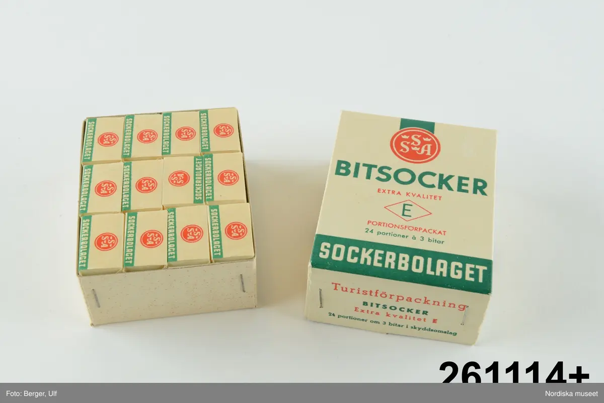 Huvudliggaren år 1960: 
”Ask, av kartong, överfalsat lock, alla hörn med häftade flikar; för ’Bitsocker extra kvalitet E portionsförpackat, 24 portioner á 3 bitar. Turistförpackning. Svenska Sockerfabriks AB.’ L 9,8 cm, Br 7,4 cm, Tj 3,8 cm. Gåva den 30/8 1960 av Fru Elsa Lindberg, Stockholm.”