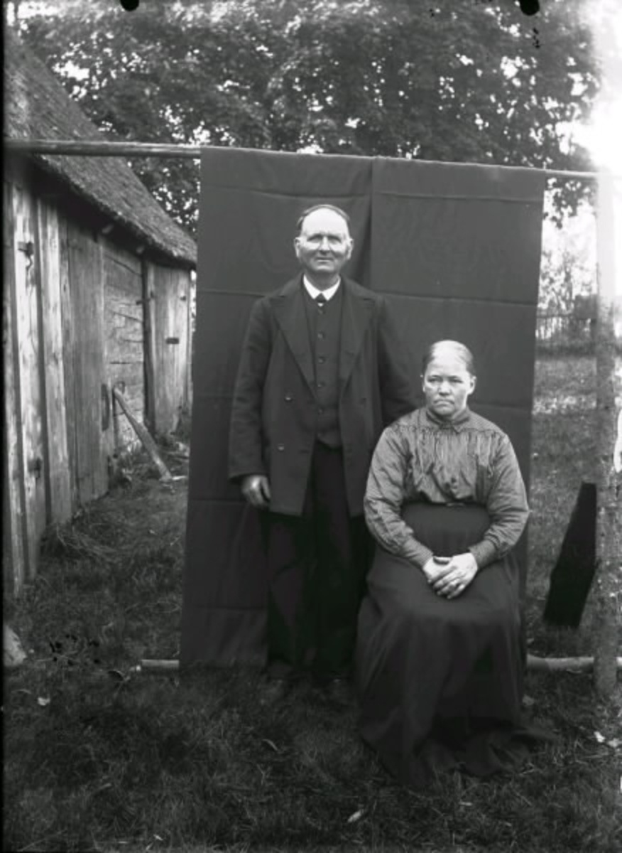 Johanna Andersdotter och Alexander Andreasson, Höghult, Drängsered. Bilden är tagen utomhus. Man har hängt ett stycke tyg över en stör som bakgrund för fotograferingen. Till vänster i bild syns en ekonomibyggnad.