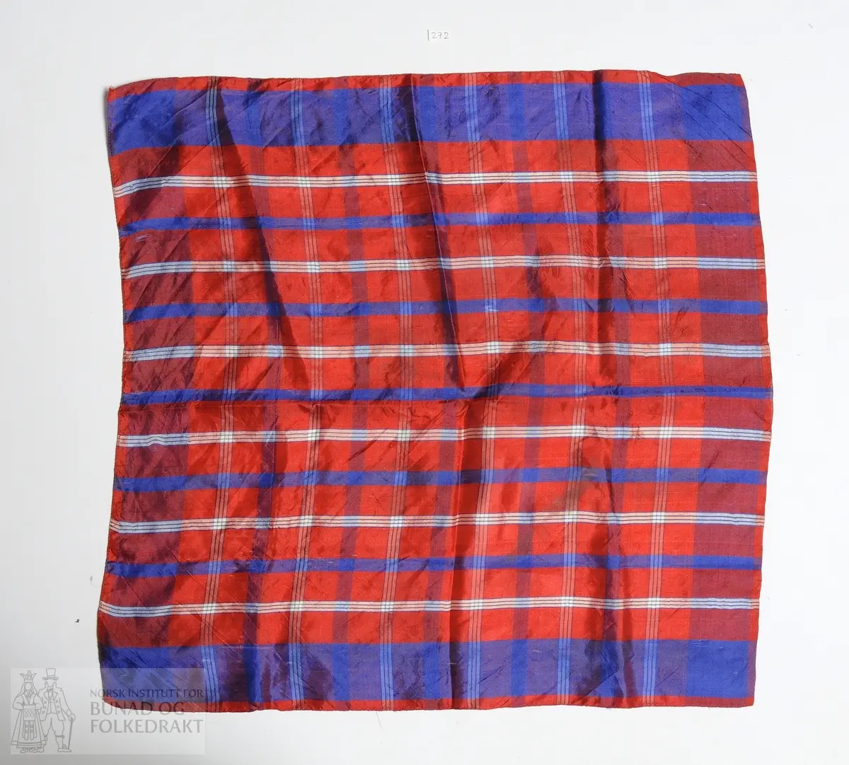 Halstørkle i silke med brede striper i rødt og blått, samt smale striper  svart og hvitt. Kypertvevd silke, faldelagt med maskin.