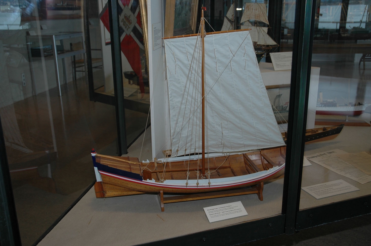 Klinkbygget  modell med løfting og ror, rorkult, 4 årer (NSM.07948-51), mast, tiljer,2 tofter. Rigget med seil. Lakket skrog, øverste bordgang malt hvit med to smalere røde linjer på hver side. Løfting blå sider. Akterspeil hvitt. Ror over vannlinjen hvitt og blått.  Målestokk 1:18.