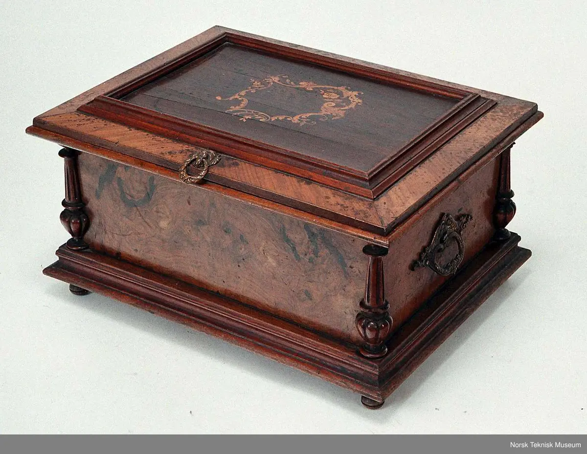 Med en plate: Die Morgenglocken. Nr. 3082. Bilde nr. 6 viser en tilsvarende spilleautomat i god stand. Den viser at det opprinnelig har vært et glasslokk over platen. På den registrerte gjenstanden er bare deler av den sorte rammen som glasset har vært festet i igjen.