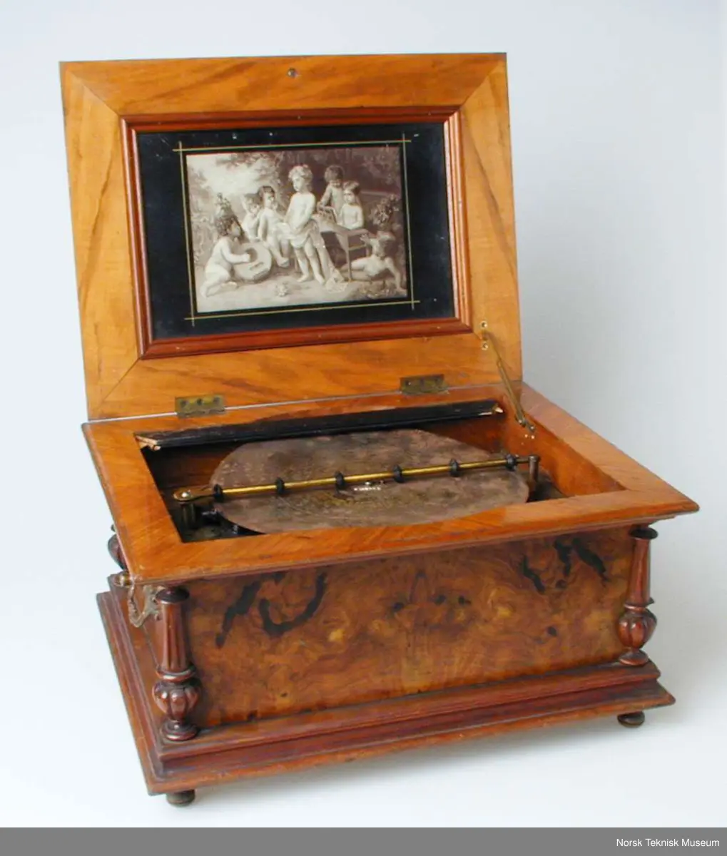 Med en plate: Die Morgenglocken. Nr. 3082. Bilde nr. 6 viser en tilsvarende spilleautomat i god stand. Den viser at det opprinnelig har vært et glasslokk over platen. På den registrerte gjenstanden er bare deler av den sorte rammen som glasset har vært festet i igjen.