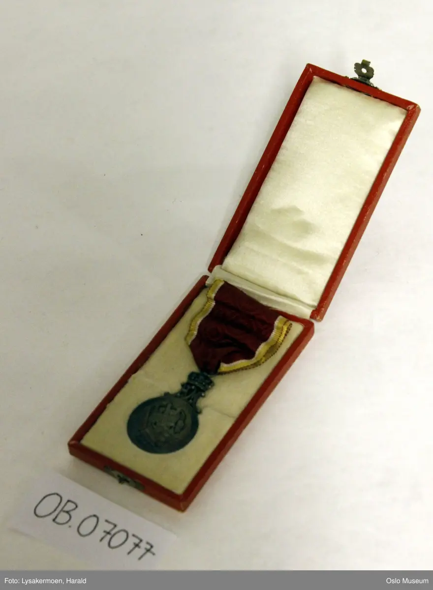 Rund medalje i bånd.

Medaljen er toppet av de sammenflettede bokstavene H og M, disse bærer en kongekrone. Båndet er festet til kronen med en sølvhempe. Båndet er rødt, kantet med hvitt, gull og rødt Medaljen er patinert - gir blåskimrende effekt.

Etuiet er av papp. Det er rødt med en gylden krone på lokket. Foret er hvitt, av silke og bomull. Forsølvet lukkemekanisme. Etuiets mål - L: 10,5 cm. B: 5,7 cm.