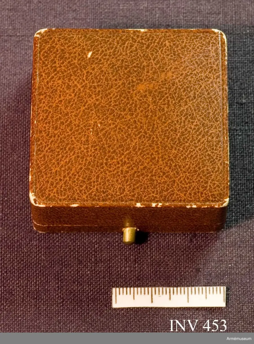 Brunt etui skänkt av fru M. Lilliehöök. Invändig botten klädd med vit sammet. Finns en springa för broschens nål. Locket invändigt klätt med vitt siden och bär en stämpel i guldtryckt: "Gustaf Möllenborg 14 Drottninggatan 14 Kongl. Hofjuvelerare. Stockholm." Över stämpeln en kunglig krona.
Samhörande nr är 452-453 och en bokgåva.