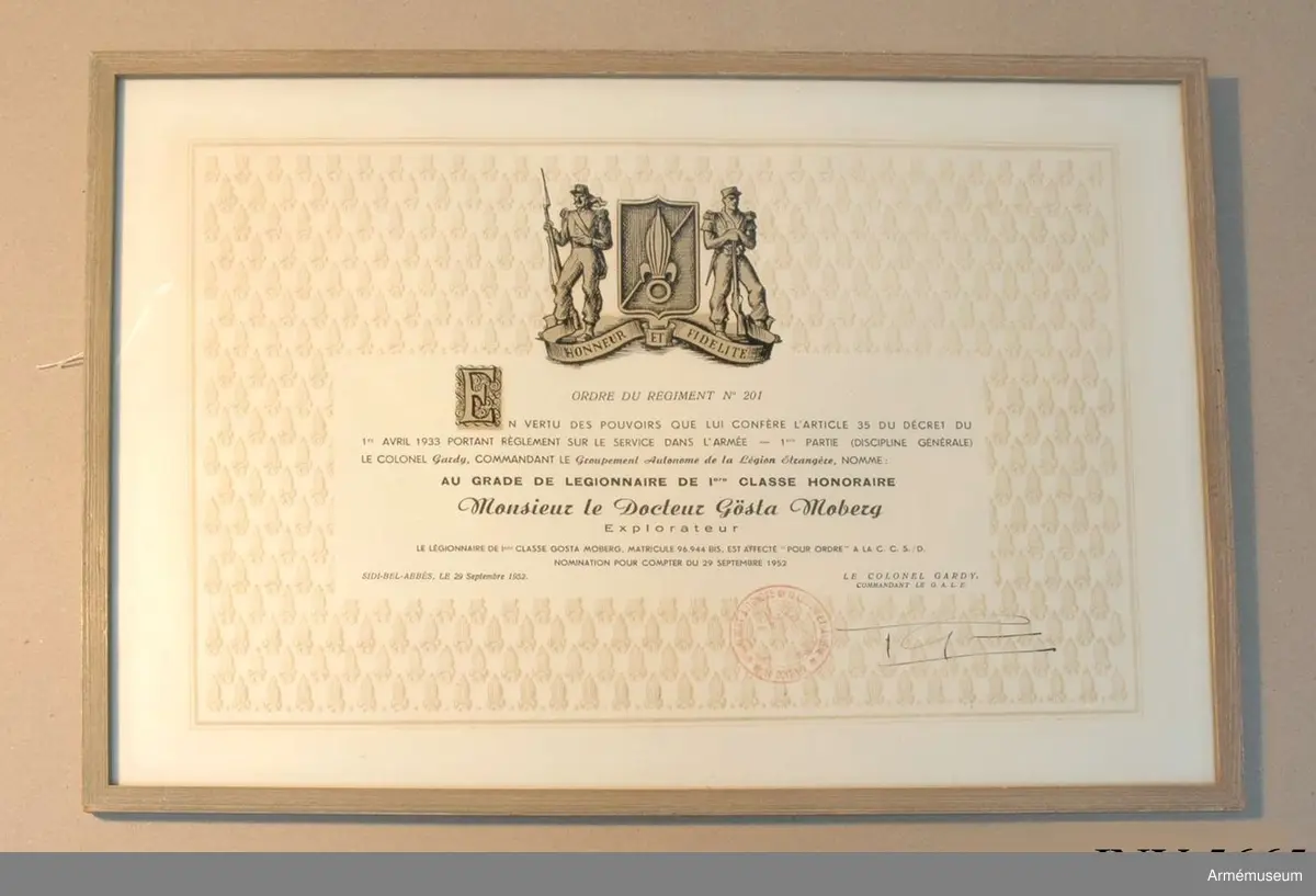 Inramad tavla. Diplom Över utnämning till "Legionere de I:ers Classe Honoraire" Honneur et Fidelite, Ordre du regiment no 201, AU GRADE DE LEGIONNAIRE ds Iere CLASSE HONORAIRE,  Monsieur le Docteur Gösta Moberg.