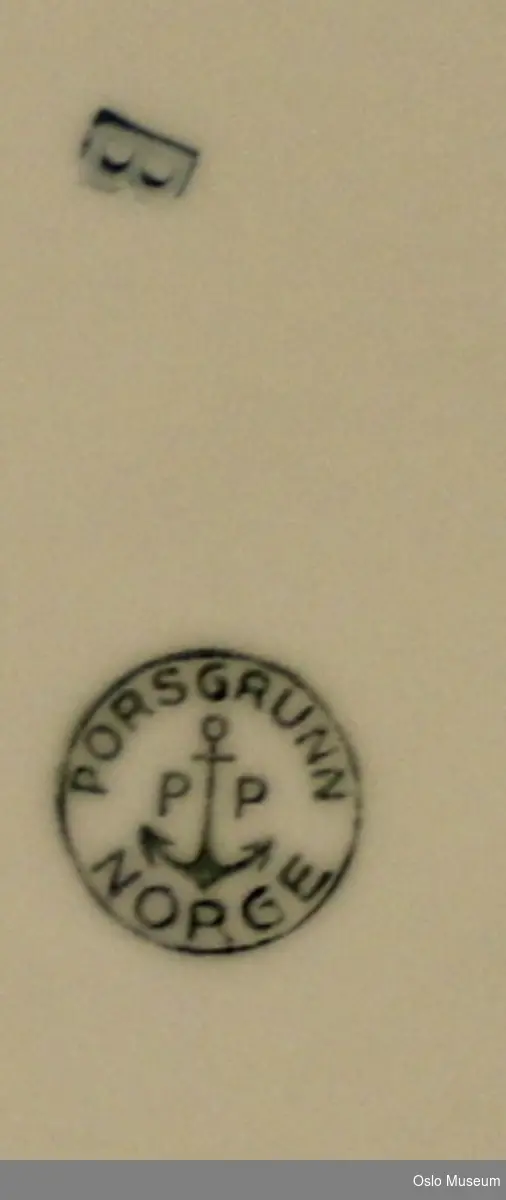 Liten hvit rund asjett med preget skrift og initialer.