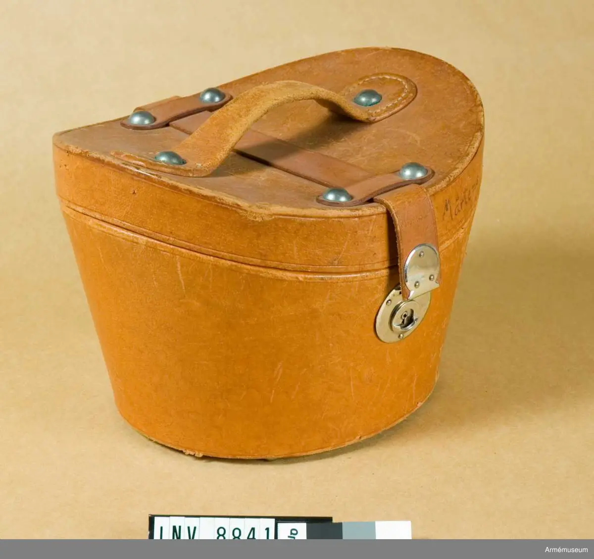 Höjd fram 160 mm. Höjd bak 160 mm. Höjd sida 190 mm.Av brunt läder formad för käppin med konkavt lock med handtag och rem som går att låsa på framsidan. Locket märkt  Mårtens A 3.