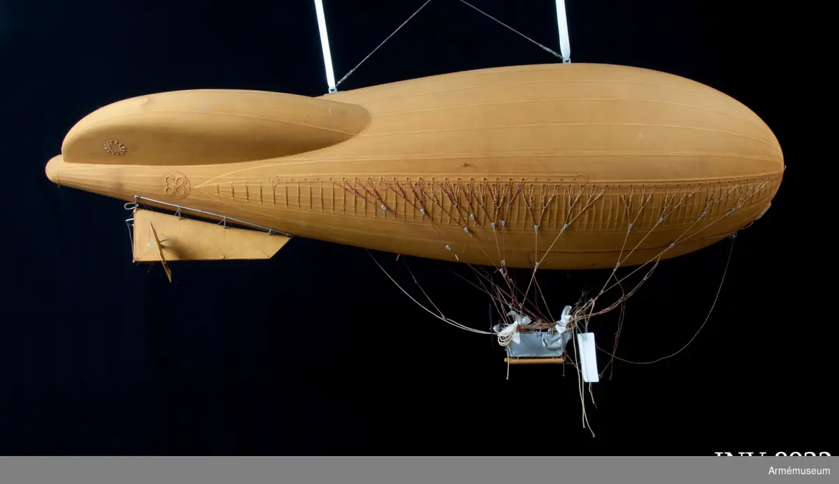 Modell av modifierad spaningsballong från ca 1928. Stora likheter med den schweiziska motoriserade M-typen av Fesselballon från samma år. Formen är långsträckt, spolformig och överklädd med gult bomullstyg av en tät kvalitet (gummiväv). Det är svårt att avgöra stommens material men det kan vara aluminium då det användes till att bygga stomme av till de "riktiga" luftskeppen. Modellen är mycket tung och därför kan det även tänkas att stommen är tillverkad av exempelvis gips. Ballongen hänger i en kraftig stålwire. Under ballongen hänger gondolen. Denna har en stomme av metall och ståltråd och är överklädd med silverfärgad väv, samt har två pontoner som "landningsställ". På ömse sidor hänger en väska. I aktern finns en propeller och på ena sidan samt mitt fram finns en ratt. Under spaningsballongens mittlinje hänger rader av linor - mitten 1 st, styrbord 4 st och babord 8 st). Dessa är mycket konstfullt utförda med s k knävringar, (styrbord 7 st, babord 10 st) fastsplitsade i ändorna. Flera linor har små öglor infästade längs med linan. Linorna är upphängda i block, - styrbord och babord har 20 st vardera. Under ballongens akter sitter balansrodret fästat varav ett roder är fast och tre är rörliga.

Se vidare Nordisk Familjebok 1912, sidan 1310, rubriken "luftskepp".