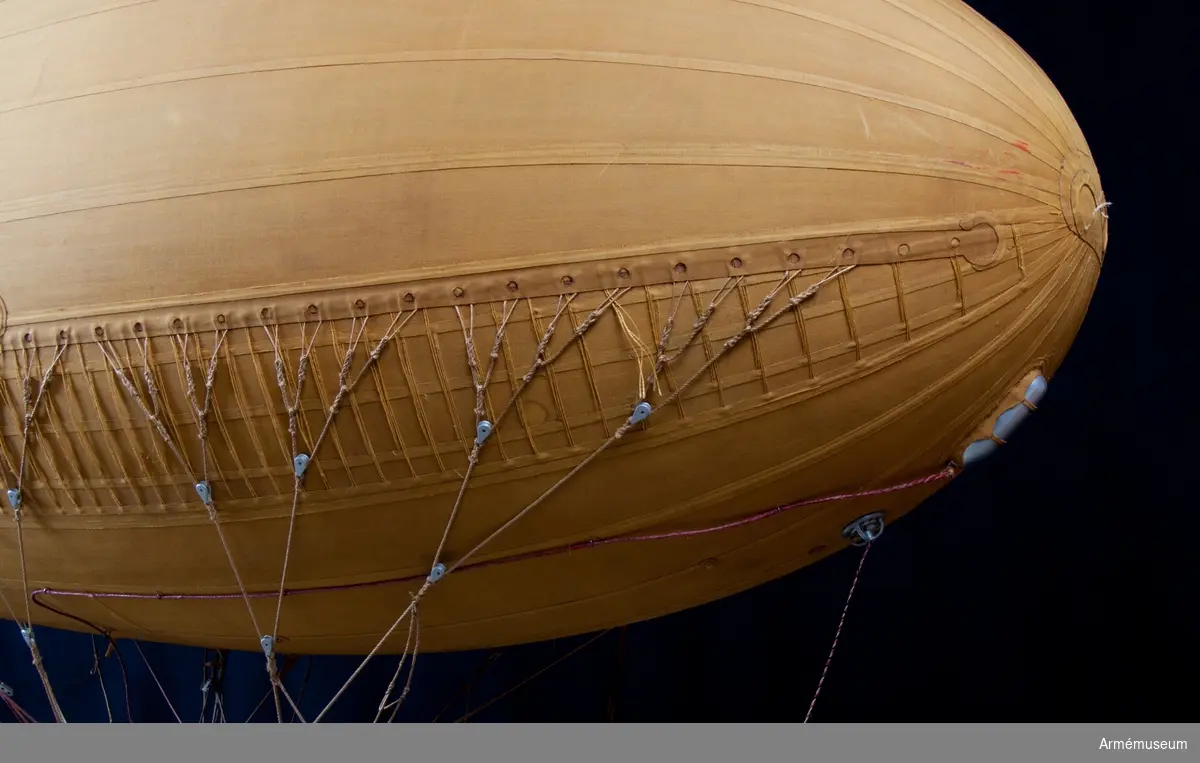 Modell av modifierad spaningsballong från ca 1928. Stora likheter med den schweiziska motoriserade M-typen av Fesselballon från samma år. Formen är långsträckt, spolformig och överklädd med gult bomullstyg av en tät kvalitet (gummiväv). Det är svårt att avgöra stommens material men det kan vara aluminium då det användes till att bygga stomme av till de "riktiga" luftskeppen. Modellen är mycket tung och därför kan det även tänkas att stommen är tillverkad av exempelvis gips. Ballongen hänger i en kraftig stålwire. Under ballongen hänger gondolen. Denna har en stomme av metall och ståltråd och är överklädd med silverfärgad väv, samt har två pontoner som "landningsställ". På ömse sidor hänger en väska. I aktern finns en propeller och på ena sidan samt mitt fram finns en ratt. Under spaningsballongens mittlinje hänger rader av linor - mitten 1 st, styrbord 4 st och babord 8 st). Dessa är mycket konstfullt utförda med s k knävringar, (styrbord 7 st, babord 10 st) fastsplitsade i ändorna. Flera linor har små öglor infästade längs med linan. Linorna är upphängda i block, - styrbord och babord har 20 st vardera. Under ballongens akter sitter balansrodret fästat varav ett roder är fast och tre är rörliga.

Se vidare Nordisk Familjebok 1912, sidan 1310, rubriken "luftskepp".