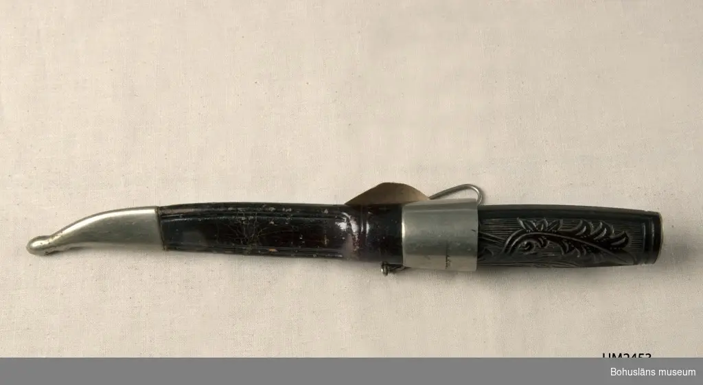 Slidkniv med skaft med graverat floralt mönster. Olika tistelliknande dekorativa ornament.
Slidan har en fästanordning kompletterat med kedja och krok att haka fast förmålet i skärp eller dylikt.

Fabriken flyttar till Sorsakoski, Finland år 1891. Sedan 1870-talets slut har företaget producerat knivar, saxar och skridskor, de s.k. Nurmiskridskorna.

Ur handskrivna katalogen 1957-1958:
Slidkniv m. ornamenterat skaft.
Kniven a) L. 16,8 cm: på bladet: "HACKMAN & Co WIBORG"; svart skaft. Slidan b) L. 15,5; läder m. beslag av metall; kort kedja m. krok. Föremålen hela.

Lappkatalog: 29