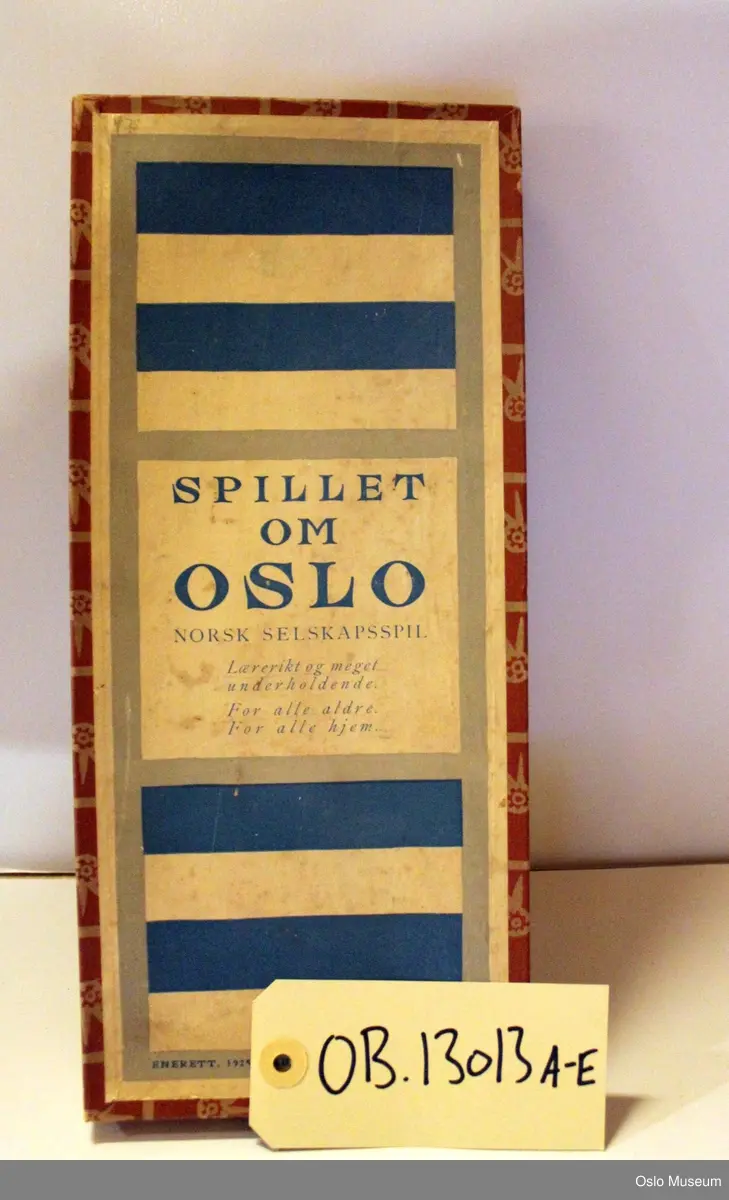 Rektangulært brettspill i eske med 72 brikker og spilleregler. Brun eske, "Spillet om Oslo" i blått på hvit bunn.
