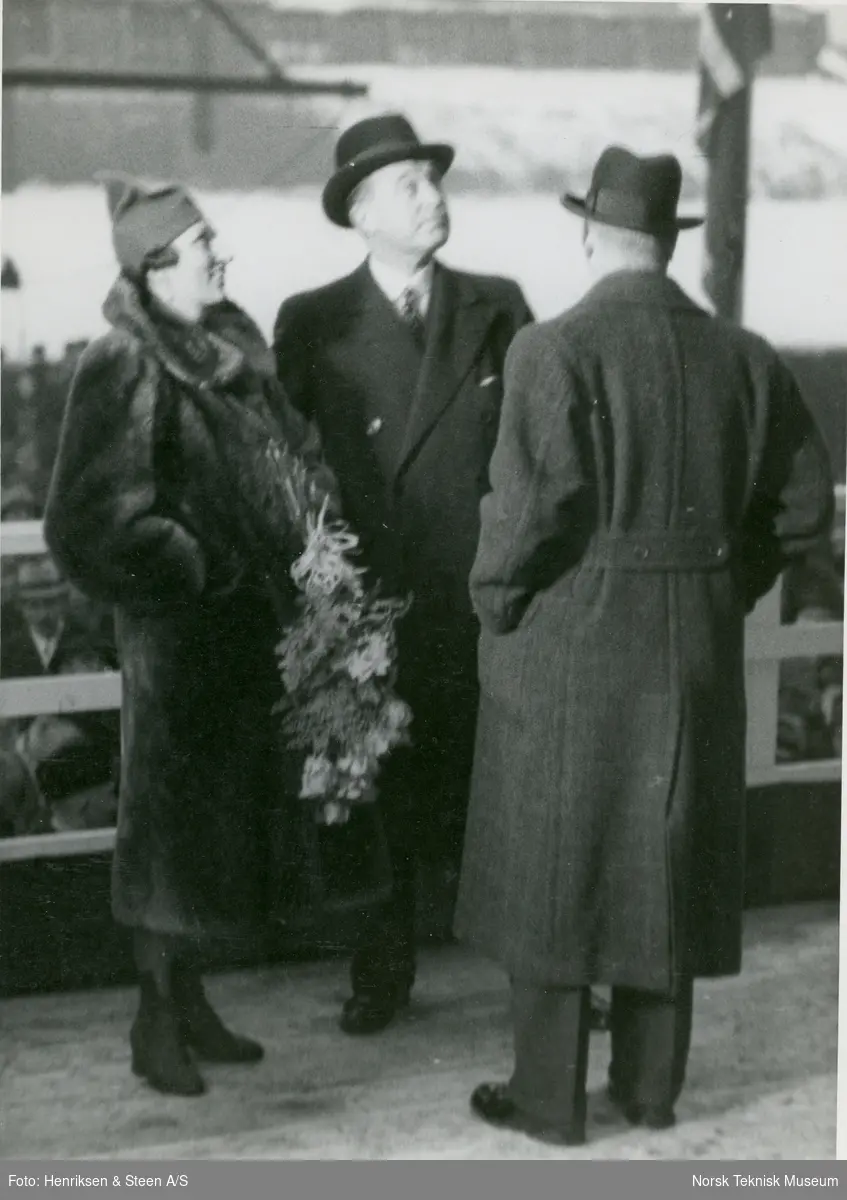 Kronprinsesse Märtha med blomstebukett sammen med Skipsreder Rudolf Olsen og adm. dir. Aamundsen på tribunen i forbindelse med dåpen og stabelavløpningen av passasjer- og lastebåten M/S Black Prince, B/N 473 på Akers Mek. Verksted 22. desember 1937. Skipet ble levert av Akers Mek. Verksted i 1938 til Fred. Olsen & Co, Oslo og gikk i rute Kristiansand - Newcastle.