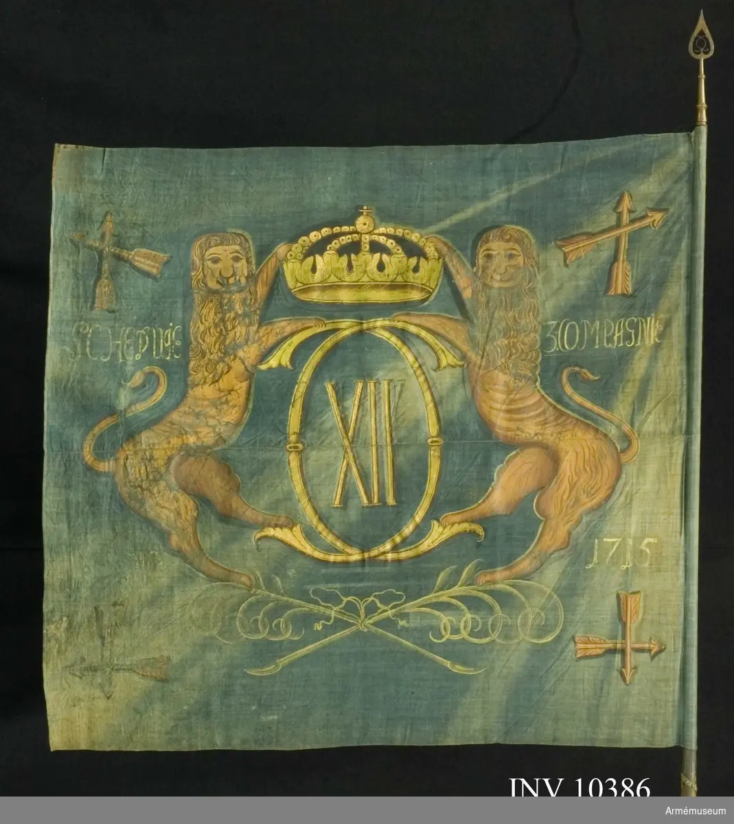 Grupp B I.
Fanduk av blå lärft, hopsydd av två våder, med målade emblem: Karl XII:s spegelmonogram av dubbelt C med XII därinom under sluten kunglig krona, hållet av två gulbruna lejon, som står på två korslagda och med bandrosett hopknutna palmkvistar i grönt. I vardera hörnet Dalarnas sköldemärke, två korslagda pilar inom korslagda palmkvistar, allt i gulbrunt och brunt.

Namnchiffret och kronan i guld, övriga emblem i gulbrunt och brunt. Fastspikad med blått linneband och mässingsspikar. Bandet lindat sex varv runt stången nedom duken. Stång av grönblåmålad furu. Spets av mässing i ett stycke, holken med  profilerade vulster. Bladet med Carl XII:s spegelmonogram i  genombrutet arbete, dess längd 29 cm.