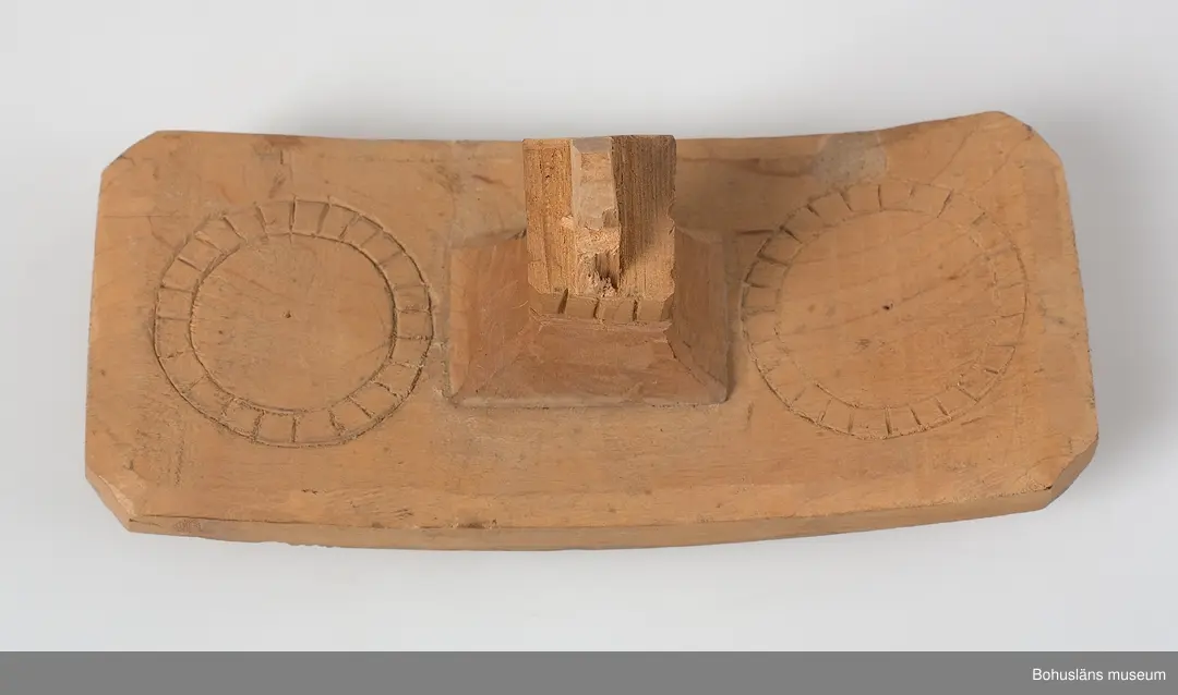 Böjd, genombruten båge med karvsnittsdekor på båda sidor bestående av rosetter. Längst ut på vardera ända är ett drakhuvud.
Rektangulära fästen, vilka vilar på hästens manke. Karvsnittsdekor med rosetter på en av dem. Den andra är sekundär och har skurna cirklar samt är defekt.
Ett drakhuvud är sekundärt.
Skadedjursangrepp.

Litteratur: Edvardsson, Ingmar, Rack, ryss och rissla, Stockholm, 1995, 
s. 66 samt bild s. 42.
Kjellberg, Sven T.: Svenska selkrokar av trä i Nordiska museet. Fataburen 1926. 
Nylén, Anna-Maja, Hemslöjd, Håkan Ohlssons förlag, Lund, 1978, s. 396-401.

Ur handskrivna katalogen 1957-1958:
Selranke av trä
I 3 delar a-c, a) = oket L. 59 cm; b) "stödplatta", L. 19,5 cm; c) d:o, L. 20 cm (nygjord). Oket har snidad dekor i genombrutet arbete m. drakhuvud i ändarna (ett nygjort); hela hela selranken har karvsnittsdekor. Omålad. Maskäten. 

Lappkatalog: 40
Hugo Hallgren var son till salteriidkaren och handelsmannen Johan Jacob Hallgren och Emelia Gerle. Företaget började sälja brissling på 1850-talet och 1864 startade man konservfabrik på Gullholmen som senare döptes till J. J. Hallgren & Söner. Sönerna var Gustav Richard, f. 1858 och Oscar Hugo, f. 1867.  Här introducerades flera nyheter inom ansjovisindustrin,  bl a Sveriges första skinn- och benfria delikatessill. Företaget var också först med att lägga in ansjovis i hermetiskt slutna kärl av bleckplåt. 1898 köptes Hallgrens konservfabrik upp av det nybildade storföretaget AB Sveriges Förenade Konservfabriker (SFK). 1901 flyttade Hugo Hallgren till Ellös där han startade en ny konservfabrik.



För uppgifter om förvärvet, se UM5155.