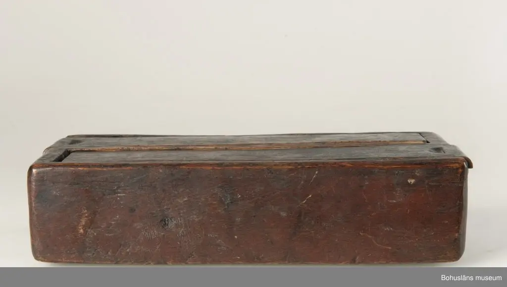 Rektangulär låda, uppdelad i två parallella fack med varsitt skjutlock upptill.
Målat med mörkt röd färg.
Inuti ett av facken finns fragment av fnöske.

Litt.; Gjaerder, Per, Esker og tiner, C. Huitfeldts förlag, Oslo, 1981, s. 48-50.

Ur handskrivna katalogen 1957-1958: 
Trälåda m. två skjutlock
a) L. 22,5 Br. 9,7, H. 5,3 cm, rödmålad; m. 2 fack, under m. ett skjutlock b) och c); deras L. 21,2 cm, Br 4 cm.

Lappkatalog: 84