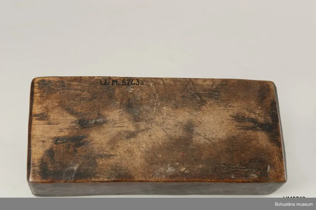 Rektangulär låda, uppdelad i två parallella fack med varsitt skjutlock upptill.
Målat med mörkt röd färg.
Inuti ett av facken finns fragment av fnöske.

Litt.; Gjaerder, Per, Esker og tiner, C. Huitfeldts förlag, Oslo, 1981, s. 48-50.

Ur handskrivna katalogen 1957-1958: 
Trälåda m. två skjutlock
a) L. 22,5 Br. 9,7, H. 5,3 cm, rödmålad; m. 2 fack, under m. ett skjutlock b) och c); deras L. 21,2 cm, Br 4 cm.

Lappkatalog: 84