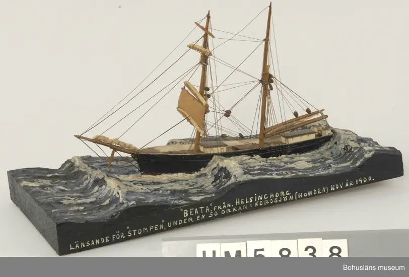 Bramsegelskonaren Beata från Helsingborg, 
Tillverkad av kapten John Emil Olsson (1880-1950), Fiskebäckskil på Skaftö i Lysekils kommun på 1940-talet.
Trä, metall, lintråd, tyg, gips.
Höjd 20 cm, längd 32 cm, B 9 cm. Platta längd 42 cm och bredd 20,5 cm. Okänd skala.
Vattenlinjemodell med två master, grönmålat skrov, röd bottenfärg, övriga detaljer vitmålade eller lackade. Stående och löpande rigg med utskurna block. Undre märssegel av snidat trä, revade segel av gasväv samt med däckshus, lastluckor och ratt. Monterad på utskuren platta med modellerad och målad gipssjö.
På plattans långsida har kapten Olsson textat med vita tryckbokstäver:
"BEATA". FRÅN HELSINGBORG 
LÄNSANDE FÖR "STOMPEN", UNDER EN SO ORKAN I NORDSJÖN (HOWDEN) NOV ÅR 1900.

Modellen föreställer hur fartyget förlorar däcklasten överbord i en orkan i Nordsjön.
I Sjöfartsbok för John Emil Olsson utfärdad vid Uddevalla Sjömanshus framgår att han var mönstrad som matros på Beata som gjorde fyra resor från Hasle på Bornholm till England via Norrland under befälhavare N. P Nilsson den 16 mars - 11 december 1901.

Definitioner:
Seglet på näst understa rån på råriggad mast kallas undermärssegel eller stump. 
Vid hårt väder beslogs fartygets alla segel utom undermärsen och man seglade "för bara stumpen". 
Blev vädret värre fick man försöka rida ut stormen och ligga bi för sviktade stumpar. Då revades halva stumpen så att bara en trekant blev kvar på rånockens ena sida.

John Emil Olsson var mönstrad på Beata  med hemmahamn Helsingborg som matros  16 mars t o m 11 december 1901 för resa  Hasle - England via Norrland (fyra resor) . 
Ur handskrivna katalogen 1957-1958:
"Beata"
Modell på platta. L. (från för till akter) 25. Föremålet helt.
Från kapten Olssons saml., Fiskebäckskil.

För ytterligare information om John Emil Olsson och förvärvet, se UM005807.

Föremålet presenterat på Bohusläns museums hemsida år 2009 - 2013, webbutställning "John Emil Olsson Fiskebäckskils sjöfartsmuseum".