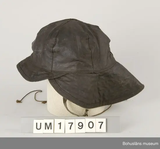 Huvudbonad vid fiske.
Hatt med kulle ihopsydd av sex trekantiga bitar. Liten skärm framtill  och en stor bak i nacken. Foder med öronlappar och snöre att knyta under hakan. Hatten är svart på utsidan och fodret beige.            
Otydlig stämpel på ena öronlappen, text: "A/S FRISTAD NR 767".         
Skärmen är större baktill för att förhindra vatten att rinna in vid  nacken.                          Ingår i redskapsbestånd ur sjöbod från Hällsö, Havstenssund, Tanum sn.
Se UM017521