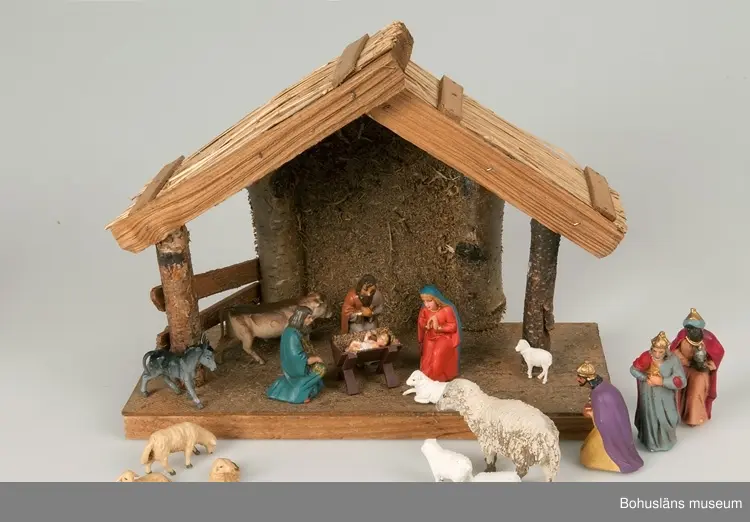 Stall med halmtak, trästolpar samt golv och vägg av masonite. Märkt UM19818:1
18 st figurer tillhör julkrubban. De är märkta UM19818:2.
Krubba, Jesusbarnet, Maria, Josef, en herde, de tre vise männen, en åsna, en oxe, tre liggande får, fem stående får varav ett betydligt större.
En av de tre vise männen märkt: Germany
Elastolin brukar denna typ av plastisk massa benämnas - egentligen ett  tyskt inregistrerat varumärke på en kompositmassa.