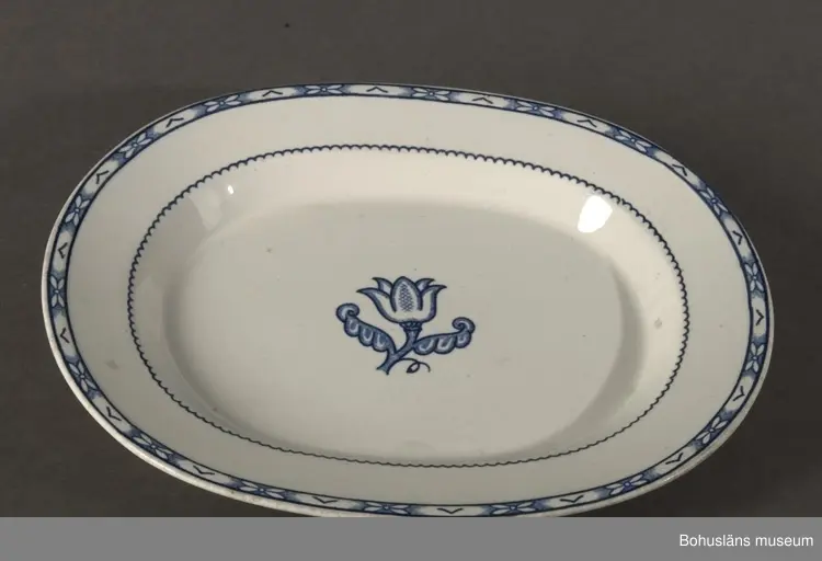 Stiliserad blå kantdekor samt tulpanliknande blomma i spegelns mitt. 
Ur servis "Holland".
Formgivare: WilhelmKåge.