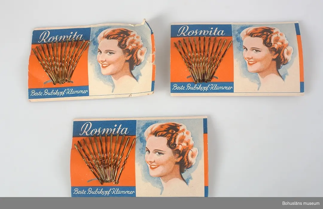 Rektangulär, pappskiva med dekor i rött, blått, vitt och text: "Rosvita. Beste Bubikopf-Klammer." 12 hårnålar av mässing isatta i solfjädersformat. Tre kartor, en skadad.