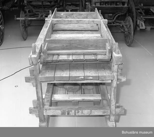 Trämangel med vagga för stenen. Två tjockare, två tunnare.
Beata Olsson  öppnade första lanthandeln i området vid Brattås, Morlanda (Henån) på 1880-talet i hus vid vägen. Mangeln uthyrdes samtidigt som lanthandeln drevs. Den var placerad i ett magasin bredvid och hyrdes av byns (Brattås) invånare. Under senare år användes den mest av
Beata Olssons släktingar. Nedmonterades något år innan den skänktes till museet.
Beata Olsson kom från Tegneby  socken. Givaren lanthandlare i Brattås.
Nuvarande affären flyttad snett över vägen längre ned i backen.