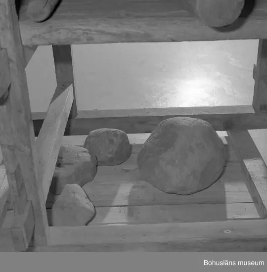 Trämangel med vagga för stenen. Två tjockare, två tunnare.
Beata Olsson  öppnade första lanthandeln i området vid Brattås, Morlanda (Henån) på 1880-talet i hus vid vägen. Mangeln uthyrdes samtidigt som lanthandeln drevs. Den var placerad i ett magasin bredvid och hyrdes av byns (Brattås) invånare. Under senare år användes den mest av
Beata Olssons släktingar. Nedmonterades något år innan den skänktes till museet.
Beata Olsson kom från Tegneby  socken. Givaren lanthandlare i Brattås.
Nuvarande affären flyttad snett över vägen längre ned i backen.