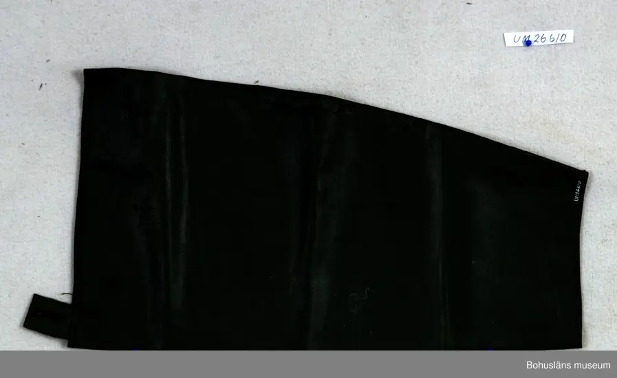 Grön avlång ärm. Upptill är det en grön stropp med ett knapphål.  Att dra utanpå skjorta som skydd för väta.
Denna typ av mudd såldes av Torvald Strannes skeppshandel på Smögen.

Övrig historik; se UM026422