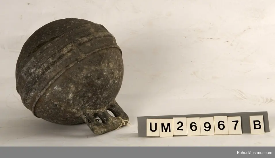 Fem klotformade flöten av metall (aluminium eller zink?). Beskrivningar av flötena i storleksordning följer här:
1. Omkrets 64 cm, med tre upphöjda ränder runtom på mitten och korta upphöjda ränder på tvären mellan dem på några ställen. I utstickande rektangulär del med rundade hörn finns två runda hål bredvid varandra. Text i relief: MANUFACTURERS PHILIPS ...(Oläsligt) TRAWL PRODUCTS GRIMSBY? ENGLAND ? (Svårlästa ord). Oläslig text p g a att den är bortsliten även på ytterligare ett ställe. Slitet.
2. Omkrets 63,5 cm, med sju upphöjda ränder, den mittersta bredare än de övriga. Två rundade metallöglor med gemensam mittdel sticker ut. Text i relief: AUTRIEB ? (Svårläst)...(Oläsligt) Märke som ser ut som ett kantigt stort S och siffrorna 197. Mycket smutsigt, fläckvis vit beläggning.
3. Omkrets 63 cm, slät yta utan upphöjningar, målad i vitaktigt grönblått i två olika nyanser, färgen delvis avsliten. Utstickande del med två närmast fyrkantiga hål. Text i relief: ... (Oläsligt ord) DE ... (Oläsligt ord) PARIS. Stor rostfläck. Mycket slitet.
4. Omkrets 55,5 cm. Med fem upphöjda ränder runtom. Rundad del med två kvartcirkelformade hål sticker ut. Text i relief: MADE IN SPAIN LA CORONA, bild av en fyr med ljusstrålar samt patentnummer med 39 siffror i. Samma? text/bild/siffror finns på ytterligare ett ställe fast är där mer sliten. Slitet.
5. Omkrets 37 cm. En upphöjd rand på mitten, för övrigt slät yta. En ögla sticker ut på ett ställe. Knutet runt den finns rester av snöre. Slitet. Rostfläckar m fl fläckar.

För uppgifter om brukaren se UM026962
Se även Bohusläns museums arkiv, arkivnummer 389.