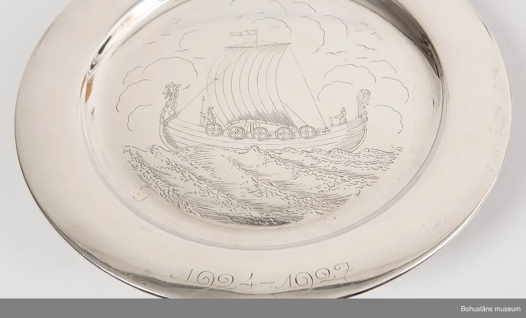 Rund tallrik  av pressad silverplåt med svagt rundat bräm. På tallrikens spegel ett graverat vikingaskepp under segel,  på brämet graverade inskriften "S. S. Vikens poängpris vid
Drakskeppspokaltävlingarne" samt årtalen 1924 - 1927, jugendstil.
På brämets baksidan stämplad med silversmed CCH; kattfot; S; Stockholms stadsstämpel samt årsbokstav V7 [1927]